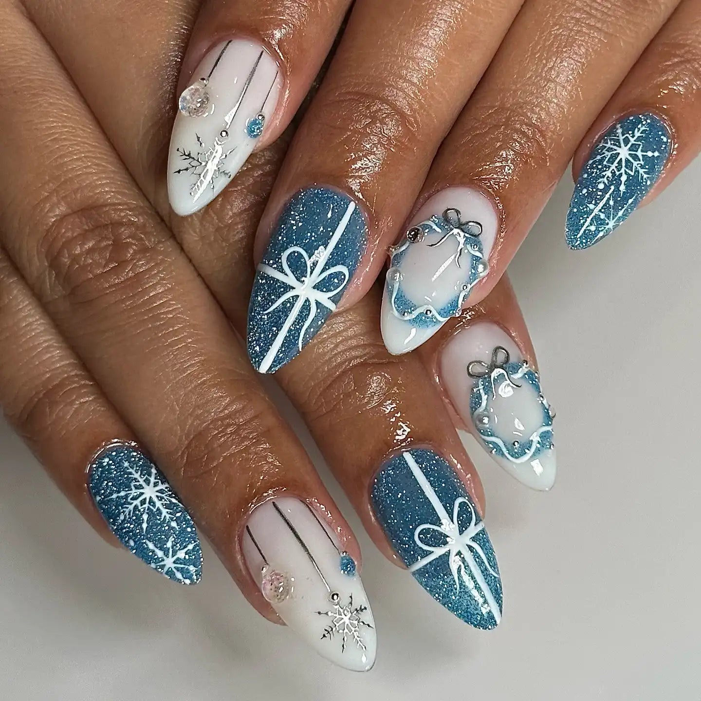 Blue and white winter holiday press-on nails with snowflakes, bows, and glitter accents