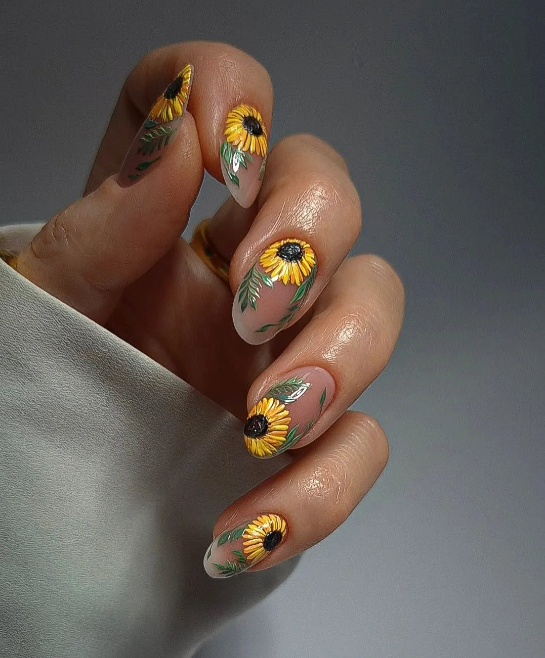 Hand with handmade press-on nails featuring yellow sunflower floral art design.
