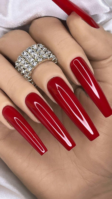 Hand with long coffin-shaped glossy red press-on nails and a rhinestone ring