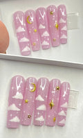 Pink press-on nails with white clouds and gold moon and star designs
