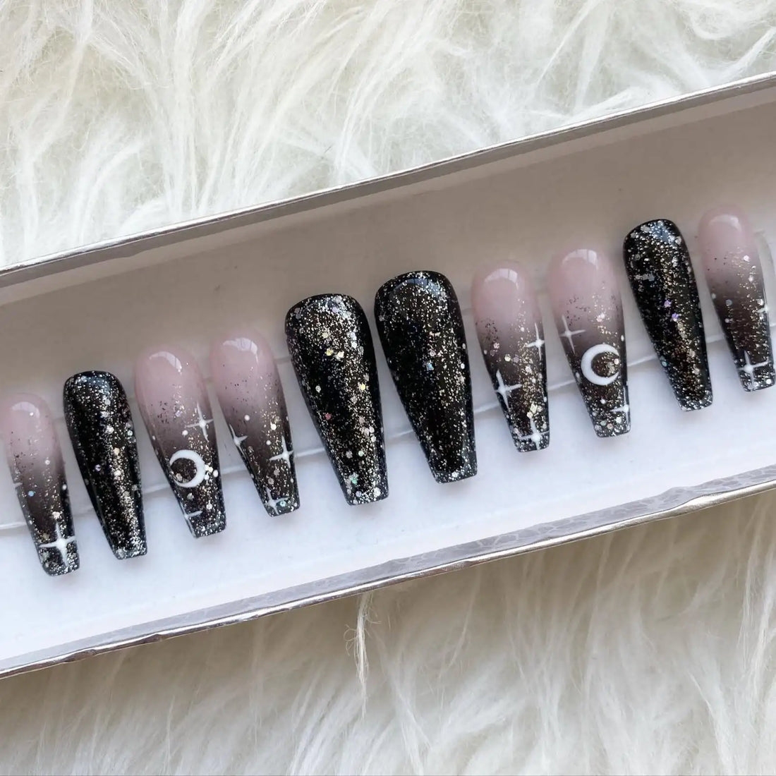 Handmade press-on nails with black ombre, glitter, moon and star designs in a box