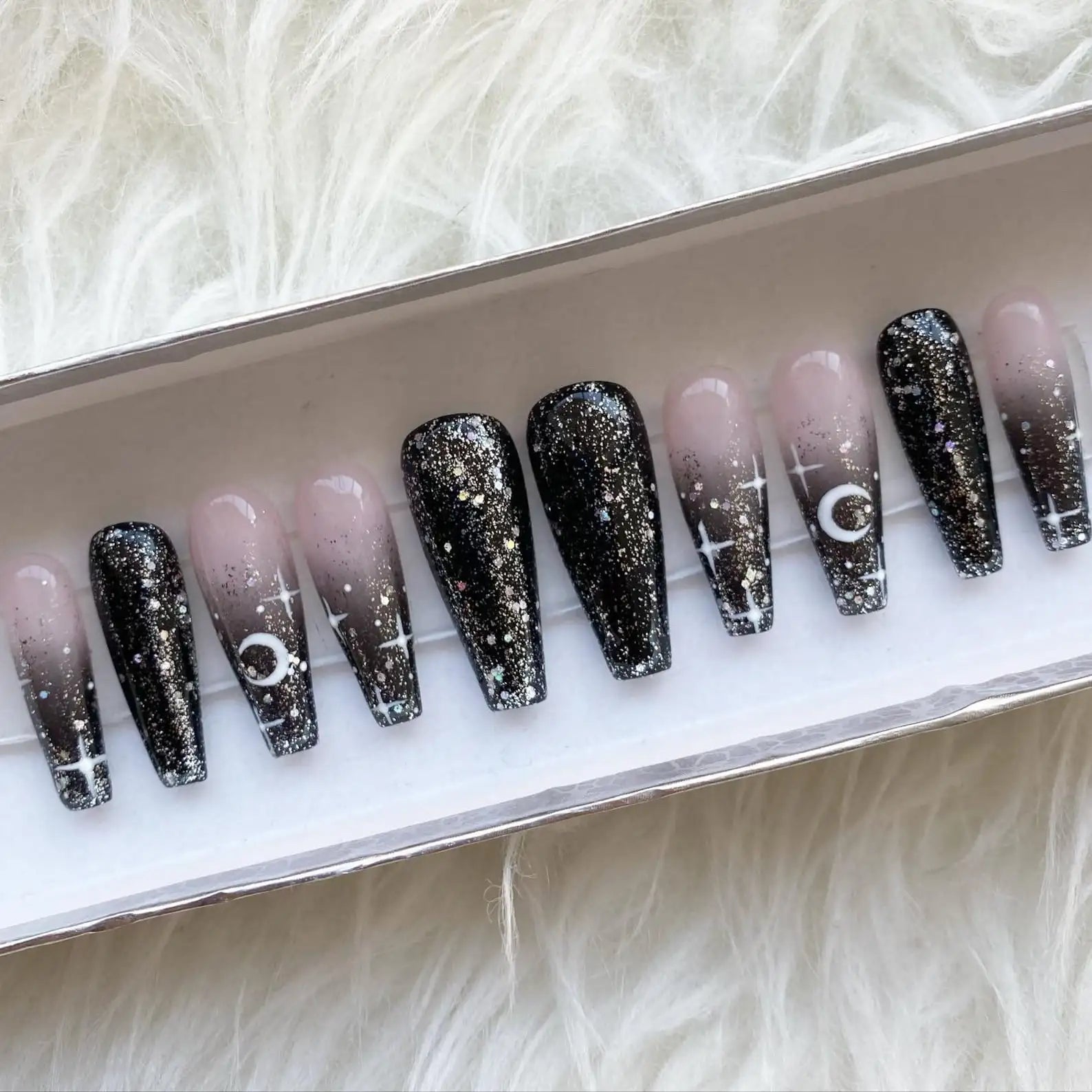 Handmade press-on nails with black ombre, glitter, moon and star designs in a box