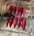 Glossy raspberry red glitter press-on nails with cat eye effect in a clear case