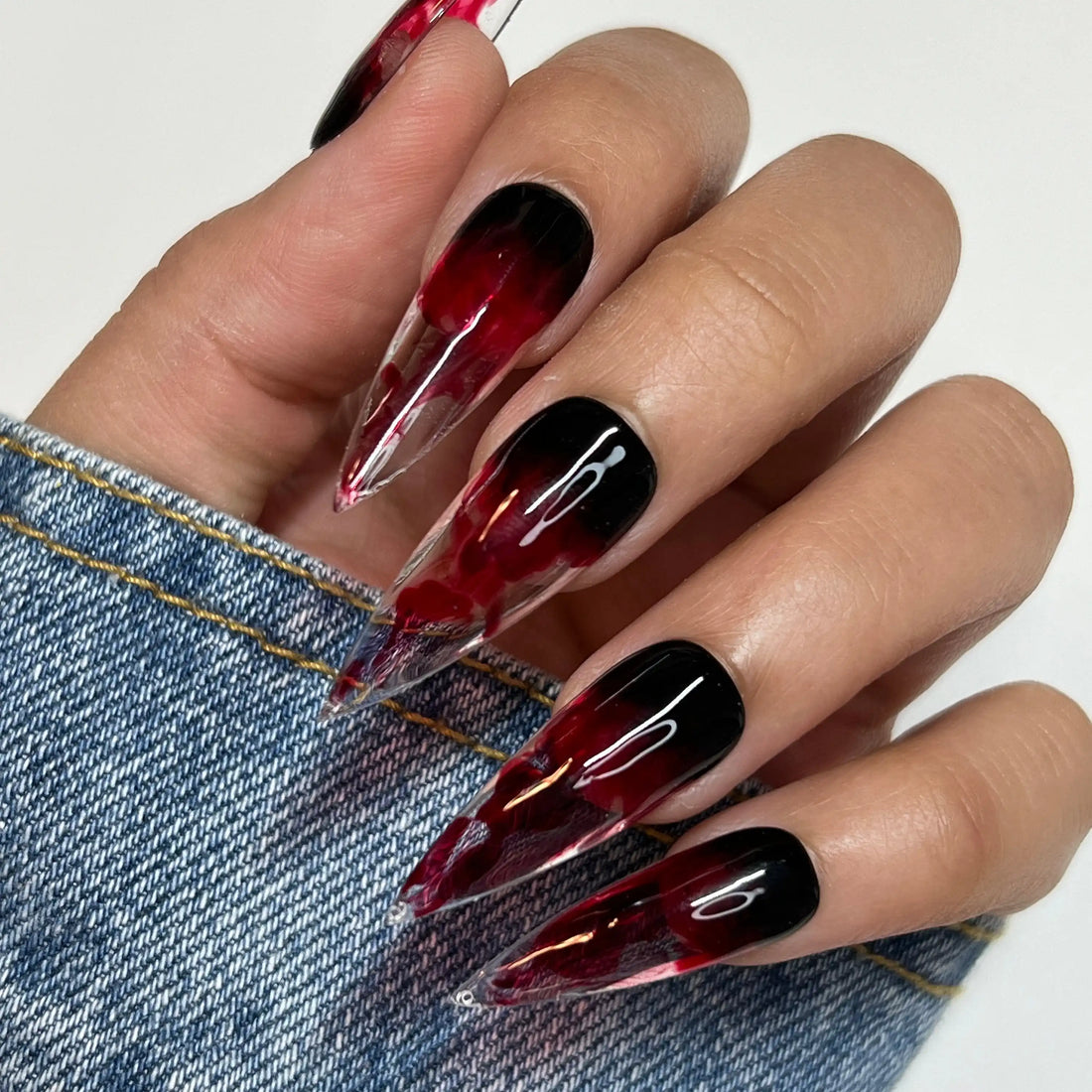 Hand with long stiletto press-on nails, black and red swirl Halloween nail art