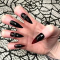 Hand with stiletto-shaped black and red ombre press-on nails, cross accents, Halloween style