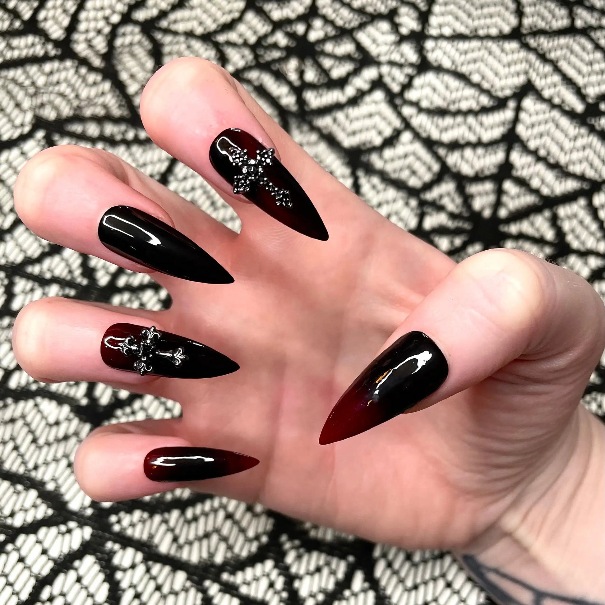 Hand with stiletto-shaped black and red ombre press-on nails, cross accents, Halloween style