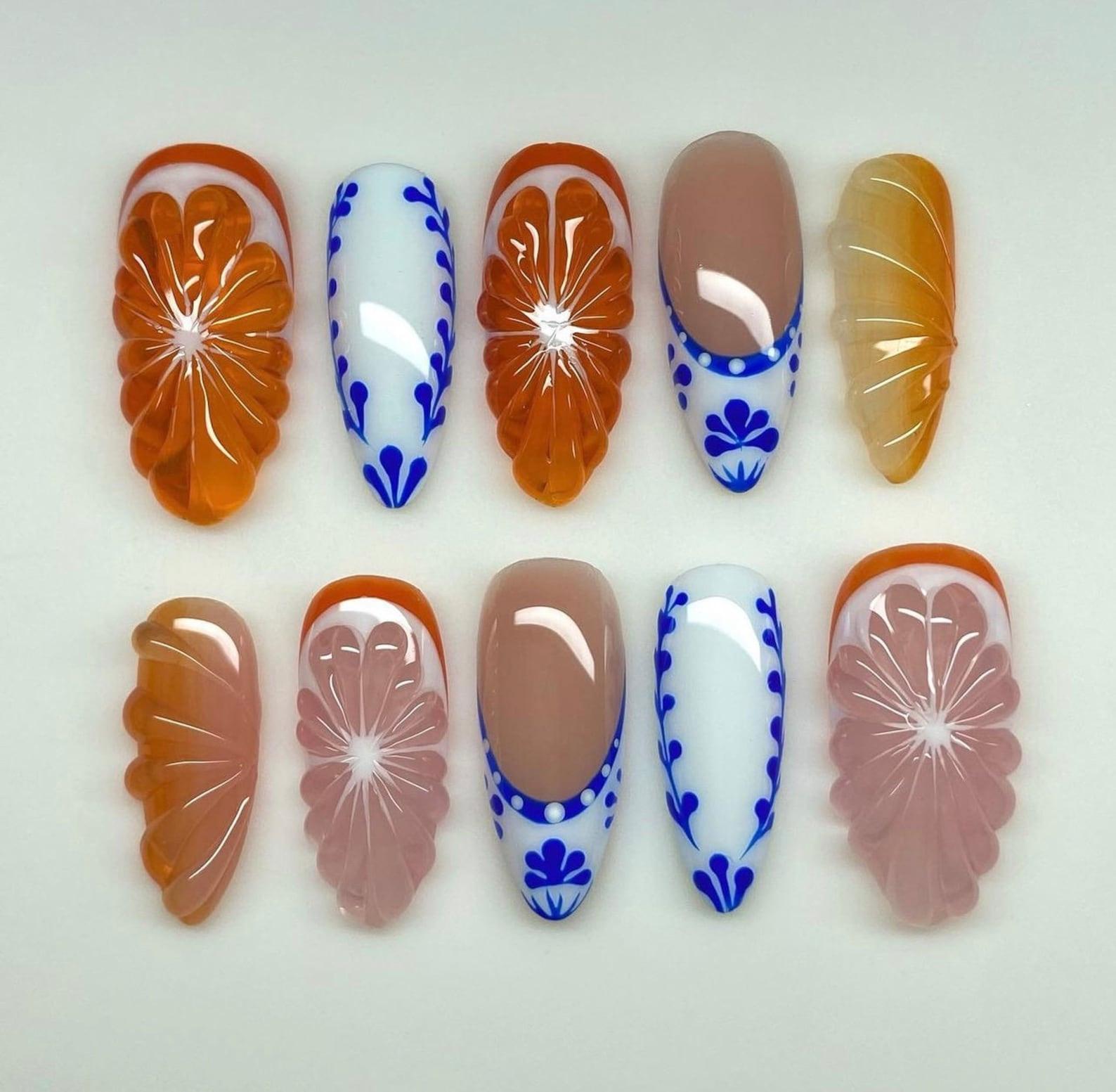 Handmade press-on nails with orange 3D floral, blue and white patterns, and glossy nude accents
