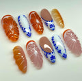 Handmade press-on nails with orange, pink, and blue floral patterns on a white background