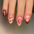 Red and nude press-on nails with cherry, ribbon, and heart nail art on almond shapes