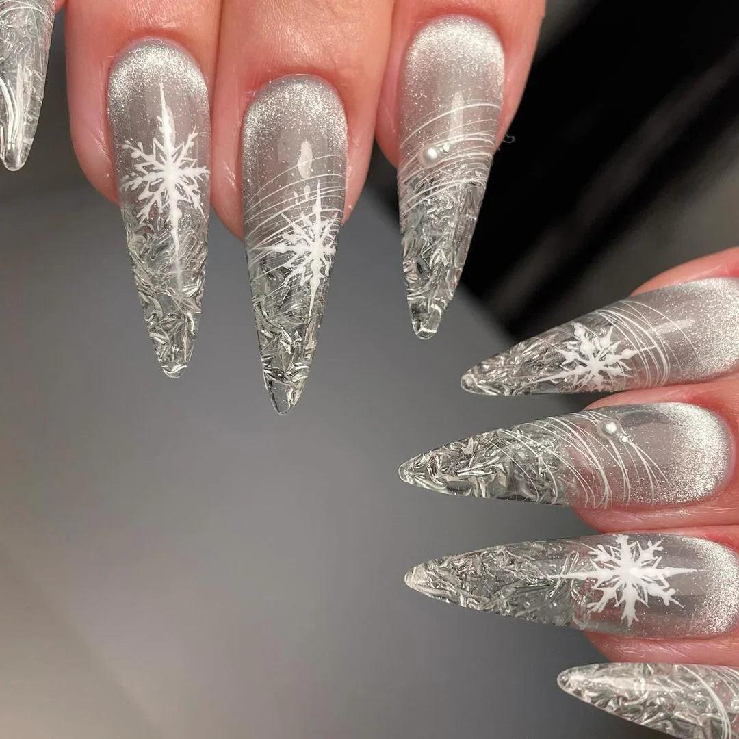 Long stiletto press-on nails with silver glitter and white snowflake nail art design