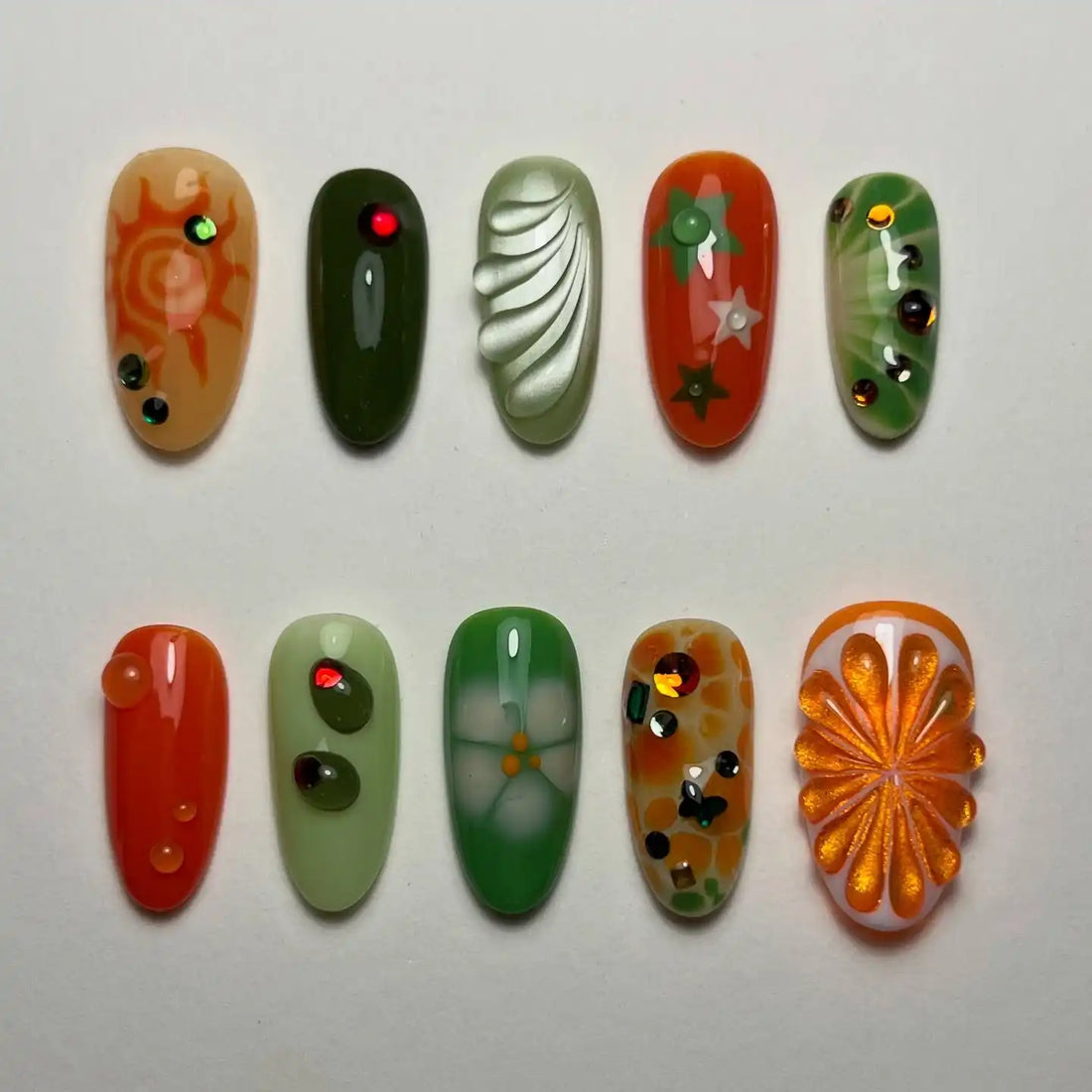 Handmade press-on nails with green and orange designs, rhinestones, and floral patterns
